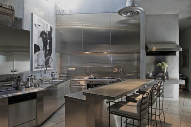 This is an example of an urban kitchen in Los Angeles with stainless steel appliances, stainless steel cabinets, stainless steel worktops, flat-panel cabinets, metallic splashback and metal splashback.