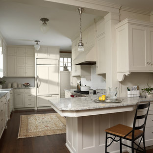 This is an example of a mid-sized victorian u-shaped eat-in kitchen in Minneapolis with a farmhouse sink, recessed-panel cabinets, white cabinets, granite benchtops, white splashback, ceramic splashback, panelled appliances, dark hardwood floors, a peninsula and brown floor.