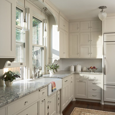 Example of a mid-sized ornate dark wood floor and brown floor kitchen design in Minneapolis with a farmhouse sink, recessed-panel cabinets, white cabinets, granite countertops, white backsplash, ceramic backsplash and paneled appliances