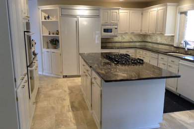 Inspiration for a mid-sized transitional u-shaped travertine floor enclosed kitchen remodel in Seattle with an undermount sink, raised-panel cabinets, white cabinets, granite countertops, gray backsplash, porcelain backsplash, stainless steel appliances and an island