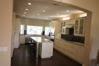 Bild på ett avskilt, stort funkis u-kök, med vita skåp, en köksö, en undermonterad diskho, skåp i shakerstil, bänkskiva i kvartsit, grått stänkskydd, stänkskydd i glaskakel, rostfria vitvaror och mörkt trägolv