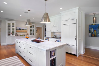Mid-sized arts and crafts l-shaped medium tone wood floor enclosed kitchen photo in New York with an undermount sink, white cabinets, marble countertops, stone tile backsplash, an island, shaker cabinets, white backsplash and white appliances