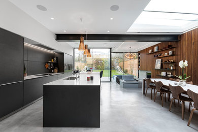 Contemporary galley kitchen in London with a submerged sink, flat-panel cabinets, black cabinets, integrated appliances, concrete flooring, an island, grey floors and white worktops.