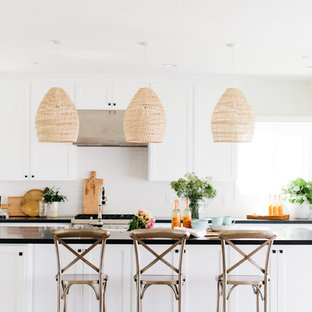 Photo of a beach style galley kitchen in San Diego with shaker cabinets, white cabinets, white splashback, medium hardwood floors, with island and brown floor.