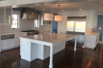 Example of a large classic l-shaped dark wood floor kitchen design in Philadelphia with recessed-panel cabinets, white cabinets, white backsplash, stainless steel appliances, an island, a farmhouse sink and quartzite countertops