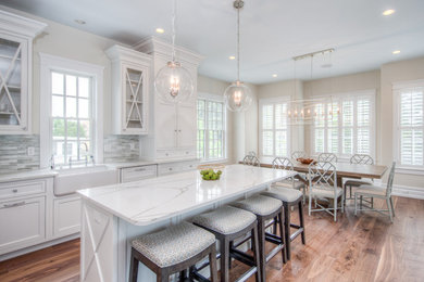 Eat-in kitchen - mid-sized transitional l-shaped medium tone wood floor and brown floor eat-in kitchen idea in Philadelphia with a farmhouse sink, shaker cabinets, white cabinets, quartz countertops, multicolored backsplash, matchstick tile backsplash, white appliances and an island