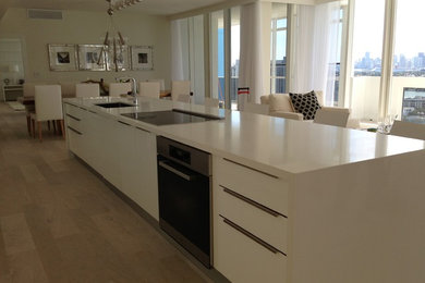 Mid-sized trendy galley light wood floor and beige floor eat-in kitchen photo in Miami with an undermount sink, flat-panel cabinets, white cabinets, solid surface countertops, stainless steel appliances and an island