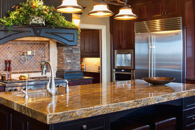 Mid-sized elegant u-shaped enclosed kitchen photo in Oklahoma City with a farmhouse sink, raised-panel cabinets, dark wood cabinets, granite countertops, brown backsplash, stone tile backsplash, stainless steel appliances and an island