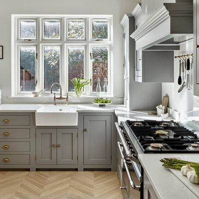 Example of a transitional l-shaped light wood floor eat-in kitchen design in London with a farmhouse sink, shaker cabinets, gray cabinets, an island and white countertops
