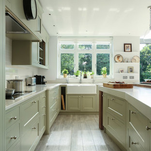 Photo of a large traditional u-shaped kitchen in London with a farmhouse sink, shaker cabinets, white splashback and with island.