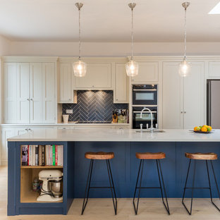 Photo of a medium sized traditional single-wall kitchen in London with a submerged sink, recessed-panel cabinets, blue splashback, metro tiled splashback, stainless steel appliances, light hardwood flooring, an island, beige floors and white worktops.