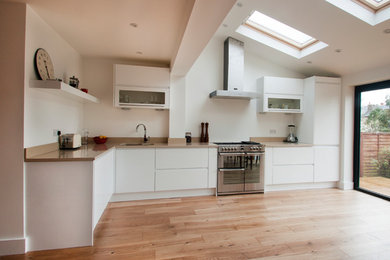 Design ideas for a small contemporary l-shaped open plan kitchen in Surrey with a built-in sink, flat-panel cabinets, white cabinets, granite worktops, stainless steel appliances, light hardwood flooring, no island and beige worktops.