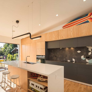 Coastal open concept kitchen appliance - Inspiration for a coastal galley medium tone wood floor open concept kitchen remodel in Phoenix with an undermount sink, flat-panel cabinets, black cabinets, blue backsplash, paneled appliances and an island