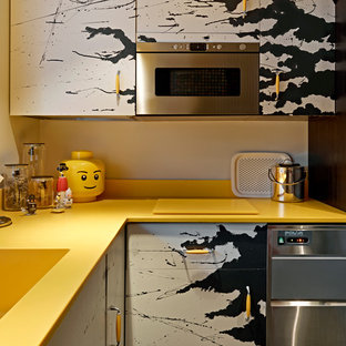 Photo of an eclectic l-shaped separate kitchen in London with flat-panel cabinets, stainless steel appliances, an integrated sink, yellow splashback, no island and yellow benchtop.