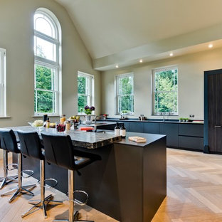 This is an example of a large contemporary u-shaped kitchen in Surrey with a submerged sink, flat-panel cabinets, black cabinets, light hardwood flooring, an island, beige floors, black worktops, beige splashback and integrated appliances.