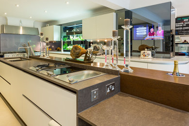 Photo of an expansive modern kitchen/diner in Buckinghamshire with flat-panel cabinets, beige cabinets, metallic splashback, glass sheet splashback, stainless steel appliances and an island.