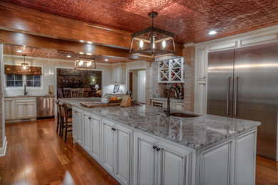 Inspiration for a timeless medium tone wood floor enclosed kitchen remodel in Other with a farmhouse sink, raised-panel cabinets, beige cabinets, granite countertops, beige backsplash, porcelain backsplash, stainless steel appliances, an island and beige countertops