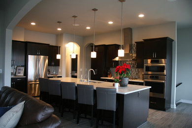 Example of a mid-sized trendy l-shaped medium tone wood floor and gray floor open concept kitchen design in Milwaukee with a single-bowl sink, flat-panel cabinets, black cabinets, quartzite countertops, gray backsplash, matchstick tile backsplash, stainless steel appliances and an island