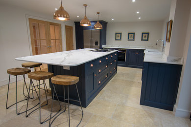 Photo of a medium sized classic l-shaped open plan kitchen in Sussex with an integrated sink, shaker cabinets, blue cabinets, composite countertops, white splashback, stainless steel appliances, limestone flooring, an island, beige floors and white worktops.