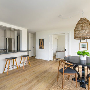 This is an example of a small modern u-shaped eat-in kitchen in Hawaii with a drop-in sink, shaker cabinets, white cabinets, soapstone benchtops, white splashback, subway tile splashback, stainless steel appliances, vinyl floors, with island, brown floor and black benchtop.