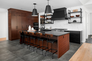 Example of an urban porcelain tile eat-in kitchen design in Toronto with an undermount sink, flat-panel cabinets, dark wood cabinets, granite countertops, white backsplash, stone slab backsplash, stainless steel appliances, an island and black countertops