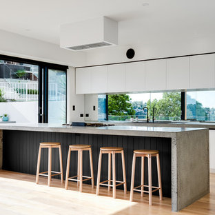 This is an example of a contemporary galley kitchen in Sydney with white cabinets, concrete benchtops, window splashback, medium hardwood floors, with island, brown floor and grey benchtop.