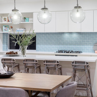 Photo of a mid-sized beach style galley eat-in kitchen in Perth with shaker cabinets, white cabinets, blue splashback, stainless steel appliances, light hardwood floors, with island, beige floor and white benchtop.