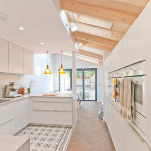 Photo of a contemporary u-shaped kitchen in Kent with flat-panel cabinets, white cabinets, white appliances, a breakfast bar, multi-coloured floors and white worktops.