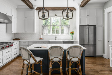 Mid-sized farmhouse l-shaped dark wood floor and exposed beam enclosed kitchen photo in Nashville with a farmhouse sink, shaker cabinets, white cabinets, quartz countertops, white backsplash, subway tile backsplash, stainless steel appliances, an island and white countertops