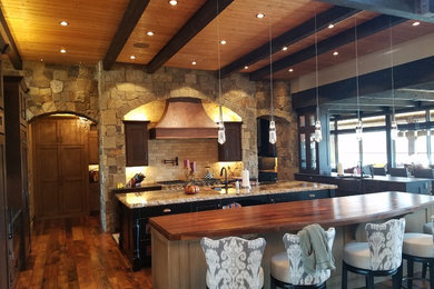 Inspiration for a large rustic galley medium tone wood floor and brown floor open concept kitchen remodel in Denver with an undermount sink, shaker cabinets, dark wood cabinets, granite countertops, beige backsplash, travertine backsplash, stainless steel appliances and two islands