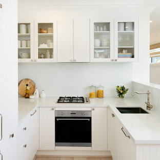 Small transitional u-shaped kitchen in Sydney with an undermount sink, white cabinets, white splashback, glass sheet splashback, no island, white floor, white benchtop and raised-panel cabinets.