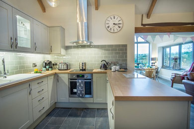 Small rural u-shaped open plan kitchen in Other with shaker cabinets, wood worktops, green splashback, metro tiled splashback and stainless steel appliances.