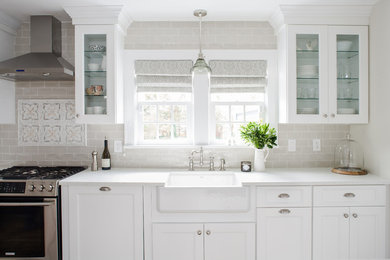 Example of a mid-sized country medium tone wood floor eat-in kitchen design in New York with a farmhouse sink, recessed-panel cabinets, white cabinets, quartz countertops, gray backsplash, ceramic backsplash, stainless steel appliances and a peninsula