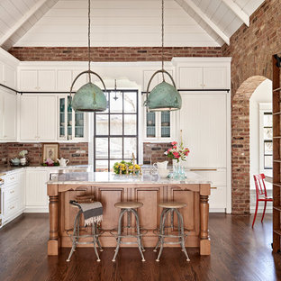 Landhausstil Wohnküche in L-Form mit Schrankfronten im Shaker-Stil, weißen Schränken, Küchenrückwand in Rot, Rückwand aus Backstein, Elektrogeräten mit Frontblende, dunklem Holzboden und Kücheninsel in Nashville