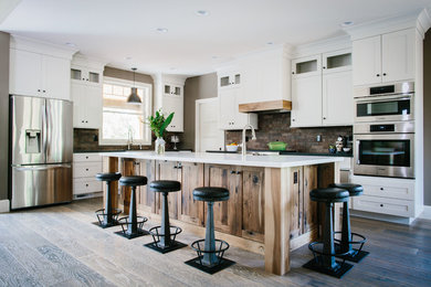 Mid-sized mountain style l-shaped dark wood floor and brown floor open concept kitchen photo in Portland with a farmhouse sink, shaker cabinets, white cabinets, quartz countertops, brown backsplash, brick backsplash, stainless steel appliances and an island