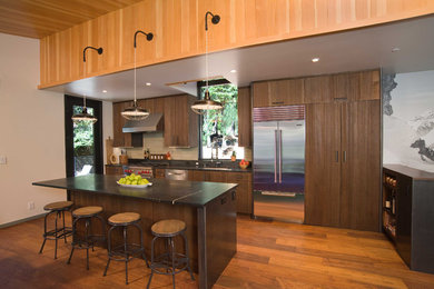 Example of a mid-sized mountain style single-wall medium tone wood floor and brown floor open concept kitchen design in Sacramento with an undermount sink, flat-panel cabinets, distressed cabinets, stainless steel appliances and an island