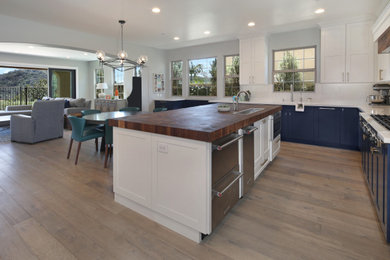Eat-in kitchen - large modern l-shaped light wood floor and beige floor eat-in kitchen idea in Orange County with a drop-in sink, shaker cabinets, white cabinets, wood countertops, white backsplash, stone slab backsplash, stainless steel appliances, an island and white countertops