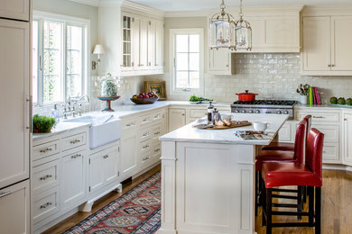 Kitchen - traditional l-shaped medium tone wood floor kitchen idea in New York with a farmhouse sink, shaker cabinets, white cabinets, marble countertops, white backsplash, subway tile backsplash, paneled appliances and an island