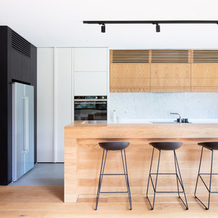This is an example of a large contemporary l-shaped open plan kitchen in Melbourne with light wood cabinets, laminate benchtops, white splashback, stone slab splashback, with island, flat-panel cabinets and grey floor.