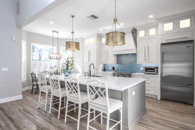 Design ideas for a medium sized contemporary single-wall kitchen/diner in Tampa with a submerged sink, shaker cabinets, white cabinets, engineered stone countertops, blue splashback, glass sheet splashback, stainless steel appliances, porcelain flooring, an island, grey floors and white worktops.