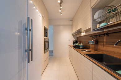 This is an example of a contemporary galley kitchen in Singapore with a double-bowl sink, flat-panel cabinets, light wood cabinets, brown splashback, white appliances, beige floors and brown worktops.