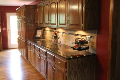 Example of a mid-sized classic light wood floor kitchen design in Kansas City with raised-panel cabinets, medium tone wood cabinets, granite countertops, beige backsplash and ceramic backsplash