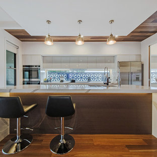 Inspiration for a mid-sized contemporary galley kitchen in Brisbane with a double-bowl sink, white cabinets, window splashback, medium hardwood floors, with island, brown floor, flat-panel cabinets, stainless steel appliances and multi-coloured benchtop.
