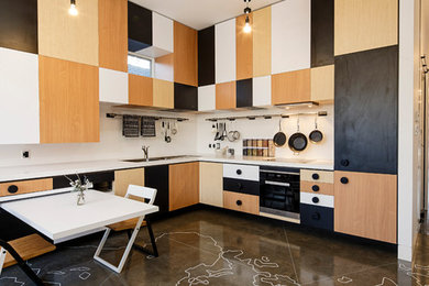 Bild på ett funkis l-kök, med vitt stänkskydd, stänkskydd i sten, svarta vitvaror och betonggolv