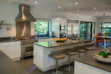 Example of a large minimalist l-shaped linoleum floor eat-in kitchen design in Austin with a double-bowl sink, flat-panel cabinets, white cabinets, solid surface countertops, gray backsplash, stainless steel appliances and an island