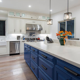 Inspiration for a mid-sized contemporary l-shaped separate kitchen in Los Angeles with a farmhouse sink, raised-panel cabinets, white cabinets, quartzite benchtops, white splashback, ceramic splashback, stainless steel appliances, light hardwood floors, with island and beige floor.