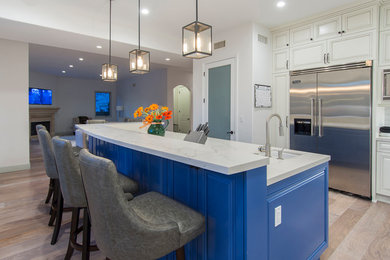 Example of a mid-sized trendy l-shaped light wood floor and beige floor enclosed kitchen design in Los Angeles with a farmhouse sink, raised-panel cabinets, white cabinets, quartzite countertops, white backsplash, ceramic backsplash, stainless steel appliances and an island