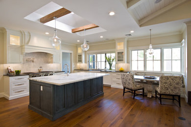 Inspiration for a large transitional u-shaped medium tone wood floor eat-in kitchen remodel in Phoenix with a farmhouse sink, recessed-panel cabinets, white cabinets, marble countertops, white backsplash, stone tile backsplash, stainless steel appliances and an island