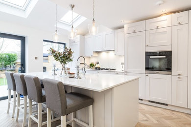 Einzeilige, Große Moderne Küche mit Landhausspüle, Schrankfronten im Shaker-Stil, Quarzit-Arbeitsplatte, Küchenrückwand in Weiß, Glasrückwand und Kücheninsel in London
