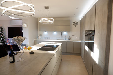 Inspiration for a medium sized modern l-shaped open plan kitchen in Other with a built-in sink, flat-panel cabinets, grey cabinets, composite countertops, white splashback, glass sheet splashback, black appliances, an island and white worktops.